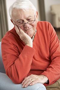 Senior Man Looking Sad In Chair At Home