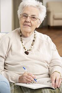 Senior Woman Relaxing In Chair At Home Completing Crossword