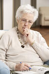 Senior Woman Relaxing In Chair At Home Completing Crossword