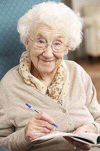 Senior Woman Relaxing In Chair At Home Completing Crossword