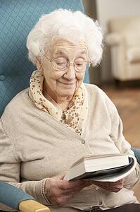 Senior Woman Relaxing In Chair At Home Reading Book