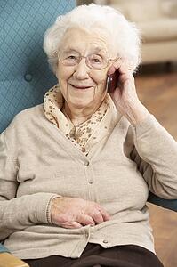 Senior Woman Talking On Mobile Phone Sitting In Chair At Home
