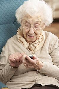 Senior Woman Dialling Number On Mobile Phone Sitting In Chair At Home