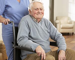 Disabled Senior Man Sitting In Wheelchair With Carer Behind