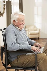 Disabled Senior Man Sitting In Wheelchair Using Laptop