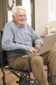 Disabled Senior Man Sitting In Wheelchair Using Laptop