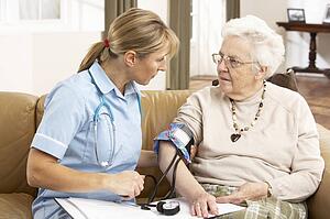 Senior Woman having Blood Pressure Taken By Health Visitor At Home