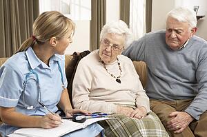Senior Couple In Discussion With Health Visitor At Home