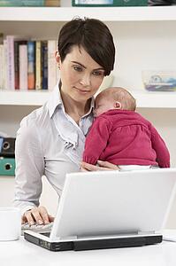 Woman With Newborn Baby Working From Home Using Laptop