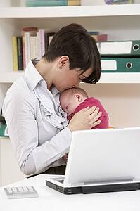 Woman With Newborn Baby Working From Home Using Laptop