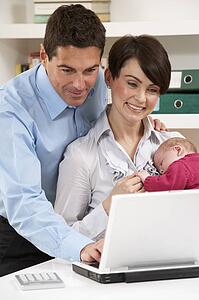 Parents With Newborn Baby Working From Home Using Laptop