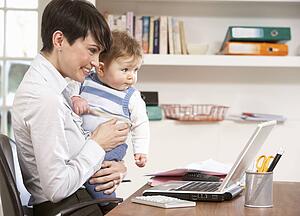Woman With Baby Working From Home Using Laptop