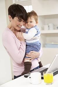 Woman With Baby Working From Home Using Laptop