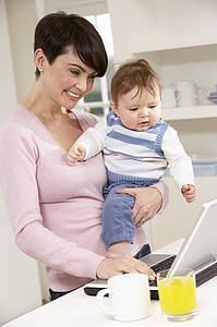 Woman With Baby Working From Home Using Laptop