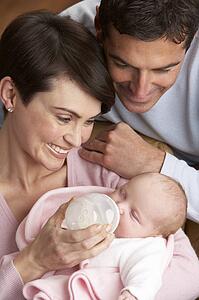 Portrait Of Parents Feeding Newborn Baby At Home