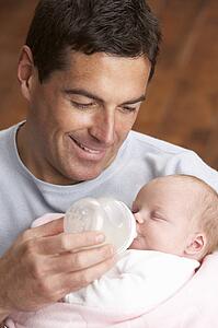Portrait Of Father Feeding Newborn Baby At Home