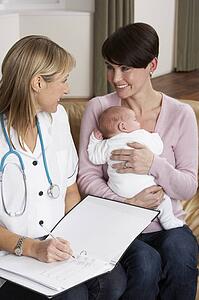 Mother With Newborn Baby Talking With Health Visitor At Home
