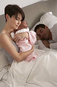 Mother Cuddling Newborn Baby In Bed At Home