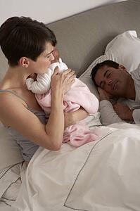 Mother Cuddling Newborn Baby In Bed At Home