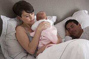 Mother Cuddling Newborn Baby In Bed At Home