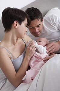 Parents Feeding Newborn Baby In Bed At Home