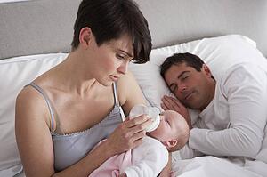 Mother Feeding Newborn Baby In Bed At Home