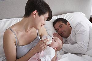 Mother Feeding Newborn Baby In Bed At Home
