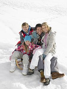Young Family Sitting On A Sled In The Snow