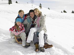 Young Family Sitting On A Sled In The Snow