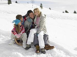Young Family Sitting On A Sled In The Snow