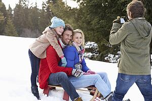 Young Family Sitting On A Sled In The Snow