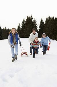 Young Family Running Through Snow With Sled