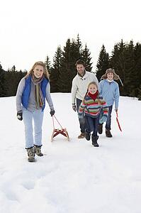 Young Family Walking Through Snow With Sled