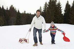 Young Father And Daughter Walking In Snow With Sleds