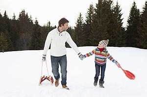 Young Father And Daughter Walking In Snow With Sleds