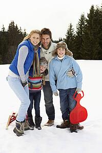 Young Family In Alpine Snow Scene With Sleds