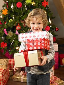 Young child holding gifts in front of Christmas tree