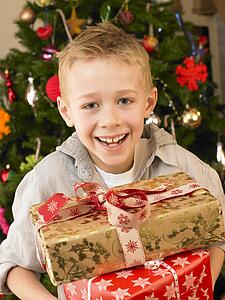 Young child holding gifts in front of Christmas tree