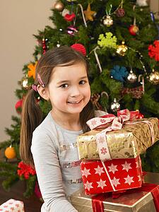 Young child holding gifts in front of Christmas tree