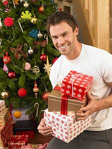 Young man holding gifts in front of Christmas tree