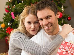 Young couple with gifts in front of Christmas tree
