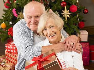Senior couple with gifts in front of Christmas tree