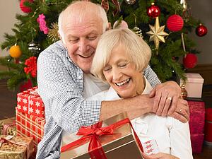 Senior couple with gifts in front of Christmas tree