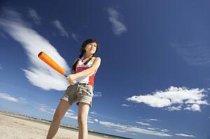 Teenage girl playing baseball on beach