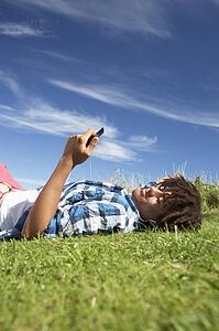 Teenage boy lying on grass with phone