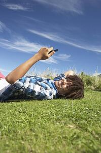 Teenage boy lying on grass with phone