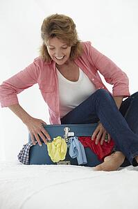 Senior woman struggling to close suitcase