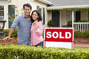 Hispanic couple outside home with sold sign