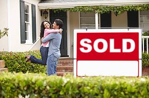 Hispanic couple outside home with sold sign