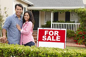 Hispanic couple outside home with for sale sign
